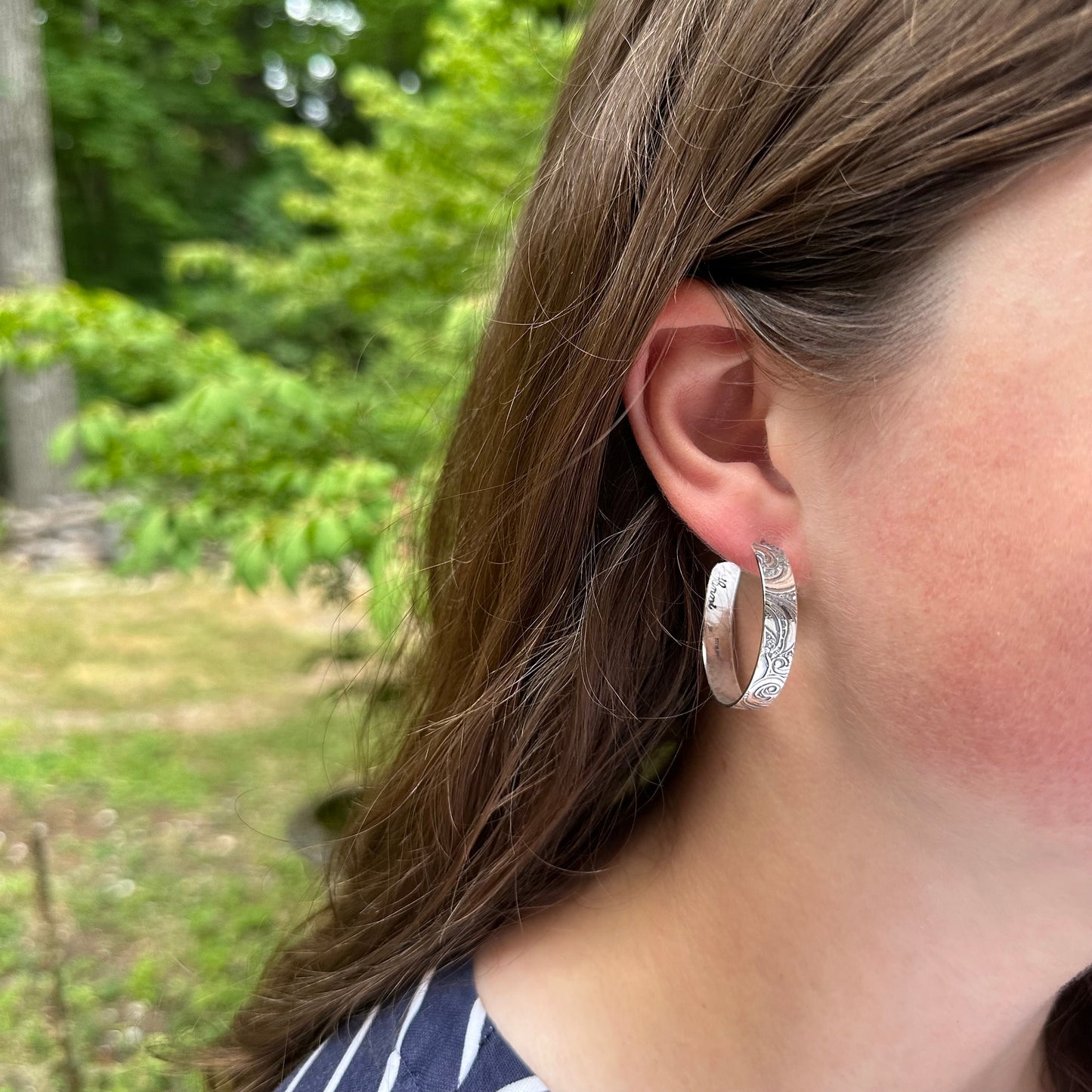 shown on model - sterling silver post hoop earring with engraved scroll pattern impressed from a vintage scroll and swirl pattern. 1/4 inch wide by your choice of diameter, handmade earrings with push back by Hanni jewelry harbor springs, Michigan